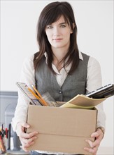 Portrait of young woman carrying office supplies in box. Photographe : Jamie Grill