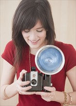 Young woman using camera, studio shot. Photographe : Jamie Grill
