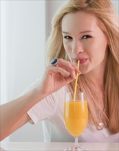 Portrait of young woman drinking orange juice. Photographe : Jamie Grill