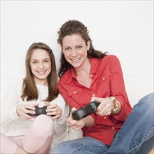 Mother and daughter (10-12 years) playing video game, portrait. Photographe : Jamie Grill
