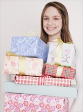 Preteen girl (10-12 years) with stack of birthday presents, smiling, portrait. Photographe : Jamie