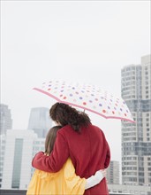 USA, New York City, mother and daughter (10-12 years) embracing under umbrella, rear view, Jersey