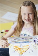 Girl (10-12) sitting on floor and showing her picture, portrait. Photographe : Sarah M. Golonka