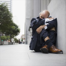Businessman wearing torn clothing, sitting on sidewalk, San Francisco, California, USA. Photographe