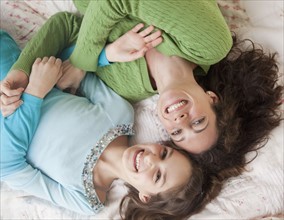 Mother and daughter (10-12 years) lying on bed, smiling, portrait, directly above. Photographe :