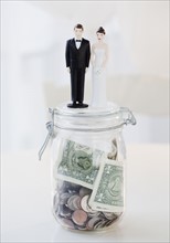 Bride and groom cake toppers on jar of money. Photographe : Jamie Grill