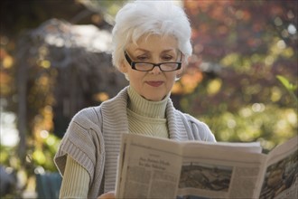 Senior woman reading newspaper outdoors. Photographe : mark edward atkinson