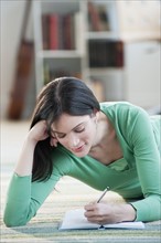 Mid-adult woman lying on floor and writing.