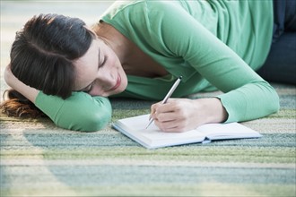 Mid-adult woman lying on floor and writing.