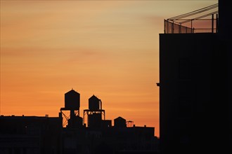 Cityscape with silhouettes of water towers at sunset, New York City, New York, USA.