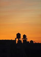 Cityscape with silhouettes of water towers at sunset, New York City, New York, USA.