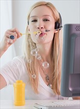 Young female telephonist blowing bubbles at work. Photographe : Jamie Grill