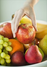 Woman's hand taking apple from fruit bowl.