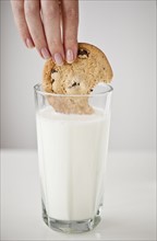 Woman's hand dipping cookie in glass of milk.