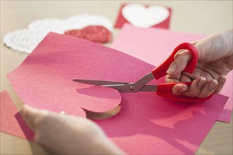 Woman cutting out heart in paper, close-up.