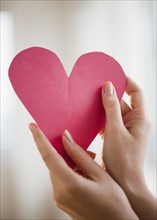 Woman holding paper heart, close-up.