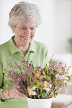 Senior woman setting flowers in vase.