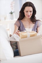 Woman unpacking parcel with present, smiling.