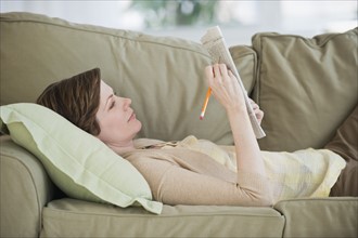 Woman lying on sofa with newspaper.