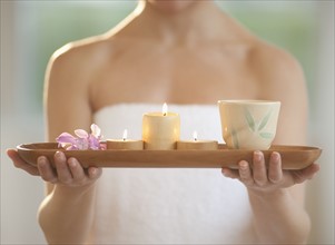 Mid-adult woman wearing towel carrying candles on tray.