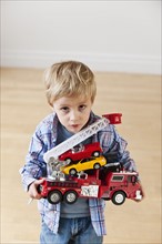 Portrait of boy (3-4) holding toy fire engine and cars.