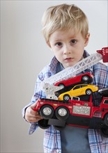 Portrait of boy (3-4) holding toy fire engine and cars.