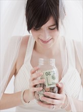 Bride holding jar of money, studio shot. Photographe : Jamie Grill