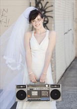 Portrait of bride holding stereo in street. Photographe : Jamie Grill
