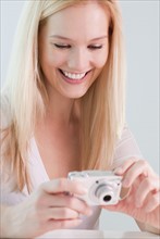 Young woman reviewing photos in digital camera, smiling. Photographe : Jamie Grill