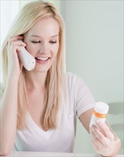 Young woman on phone, holding pill bottle. Photographe : Jamie Grill