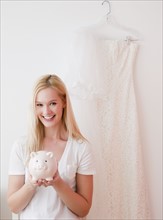 Portrait of young woman holding piggy bank with savings for wedding. Photographe : Jamie Grill