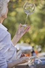 Senior woman standing in garden and examining wineglasses. Photographe : mark edward atkinson