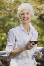 Senior woman holding glass of red wine, portrait. Photographe : mark edward atkinson