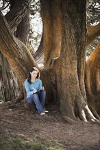 Woman writing diary by tree in park. Photographe : PT Images