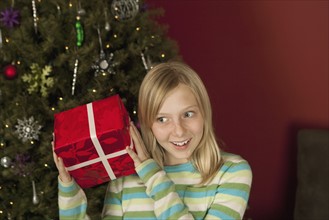 Teenage girl (10-12) shaking Christmas gift. Photographe : Sarah M. Golonka