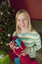 Teenage girl (13-15) holding Christmas presents in Christmas stocking, portrait. Photographe :