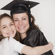 Daughter (10-12 years) embracing mother after her graduation, smiling, portrait. Photographe :