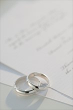 Two wedding rings on marriage certificate, studio shot. Photographe : Jamie Grill
