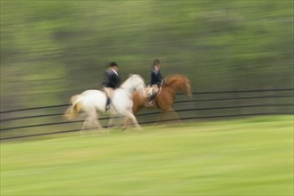 Two people riding on horses on field, blurred motion. Photographe : Stewart Cohen