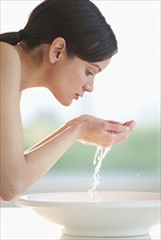 Mid-adult woman washing her face in bowl.