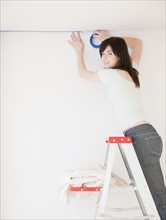 Portrait of young woman on ladder preparing to paint room. Photographe : Jamie Grill