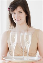 Portrait of young woman holding tray with champagne glasses. Photographe : Jamie Grill