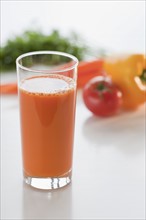 Glass of carrot juice with vegetable in background.