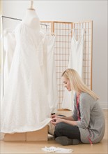 Young female tailor adjusting wedding dress in bridal shop. Photographe : Jamie Grill