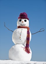 Snowman wearing hat and scarf, clear sky in background.