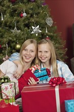 Sisters sitting in front of Christmas tree and holding Christmas gifts. Photographe : Sarah M.
