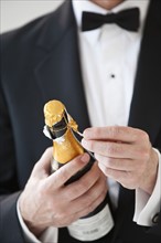 Champagne bottle being opened by a man in a tuxedo.