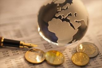 A globe on business papers with some coins.
