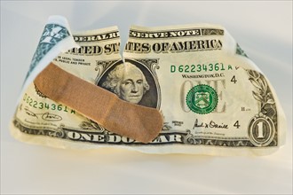 Crumpled dollar bill with a band aid