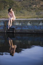 A woman sitting on a stone wall by water
